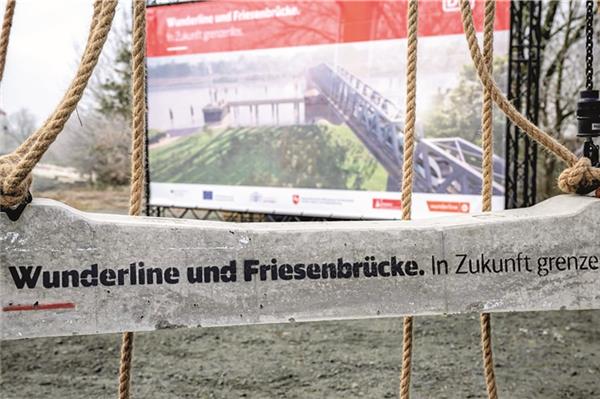 Symbolischer Auftakt in der Gemeinde Westoverledingen (Landkreis Leer): Vertreter der Bahn und der Politik hoben eine erste Bahnschwelle mit der Aufschrift „Wunderline und Friesenbrücke“ in die zu ertüchtigende Trasse. Die Brücke soll eine Landmarke werden, wenn sie ab Ende 2024 fertig ist.
